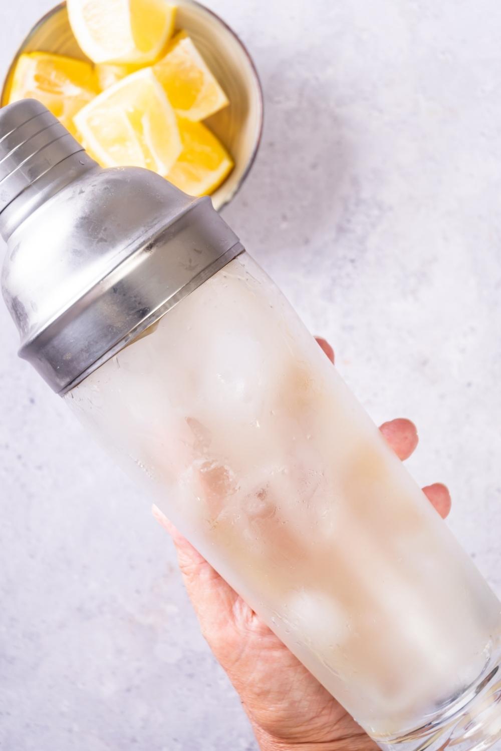 A hand shaking a cocktail shaker filled with a white tea shot.