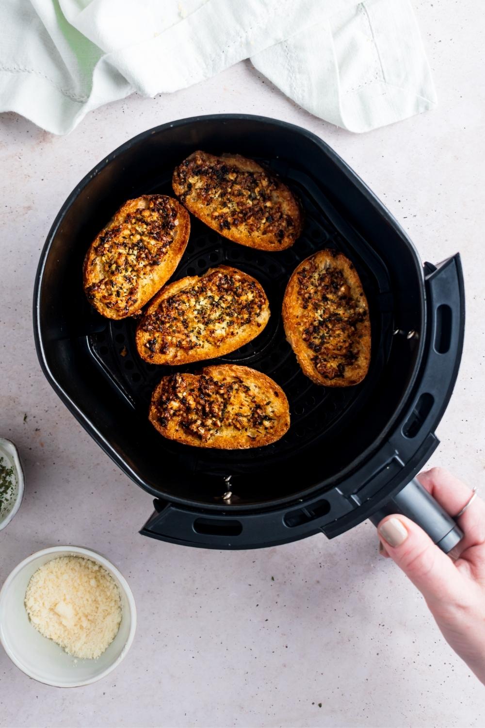 Five pieces of cooked garlic bread in an air fryer basket.