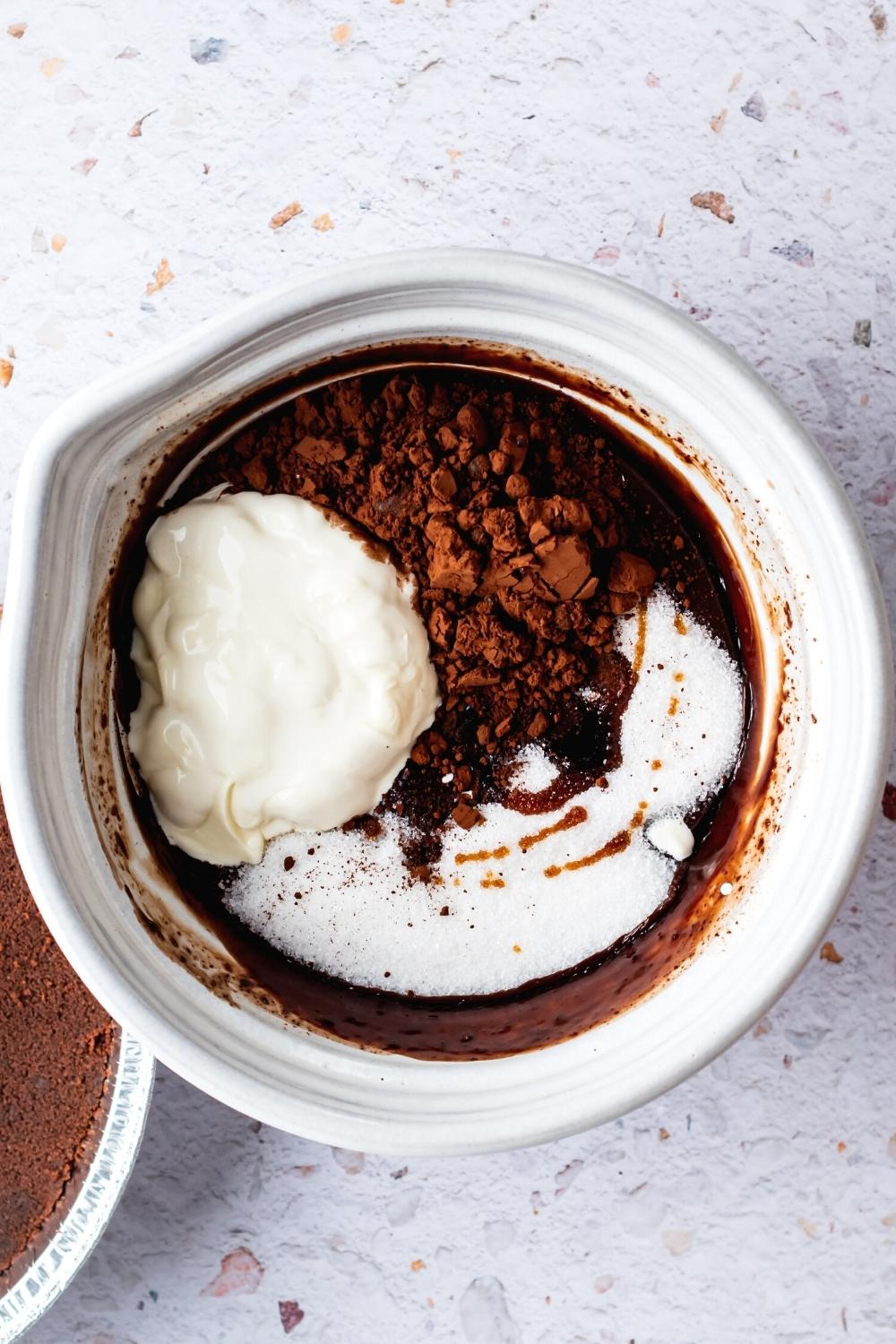 Heavy whipping cream, sugar, cocoa powder, and melted chocolate in a white bowl.