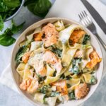 Pasta, salmon, and spinach covered in cream sauce in a white bowl.