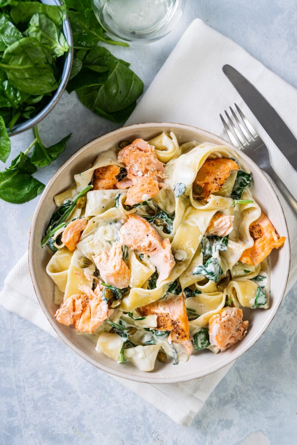 Pasta, salmon, and spinach covered in cream sauce in a white bowl.