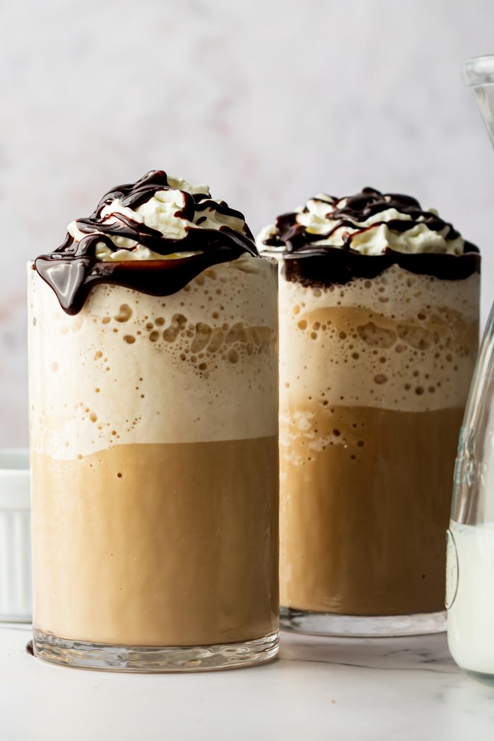Two glasses of homemade McDonald's mocha frappe's in glasses topped with whipped cream and chocolate drizzle.