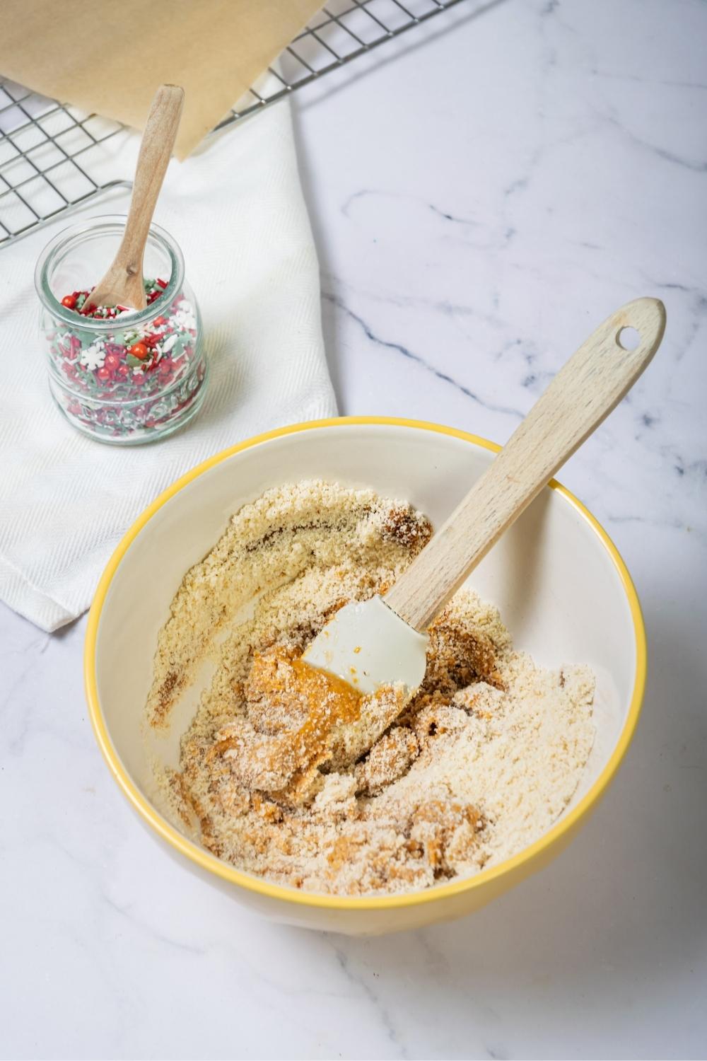 A bowl filled with peanut butter and almond flour. Behind it is a jar of christmas sprinkles.