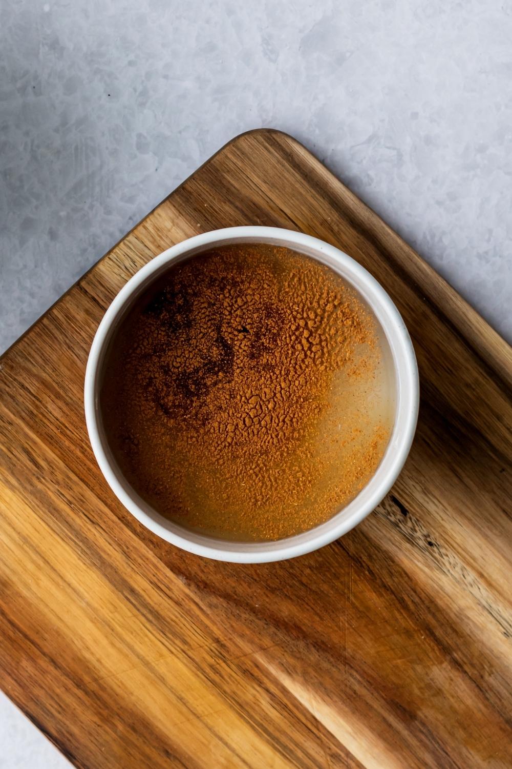 A bowl that is filled with cinnamon, water, sugar, and vanilla extract on a wooden board.