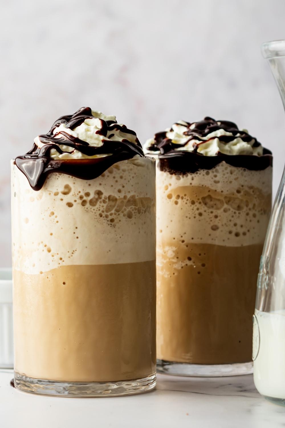 Two glasses of homemade McDonald's mocha frappe's in glasses topped with whipped cream and chocolate drizzle.