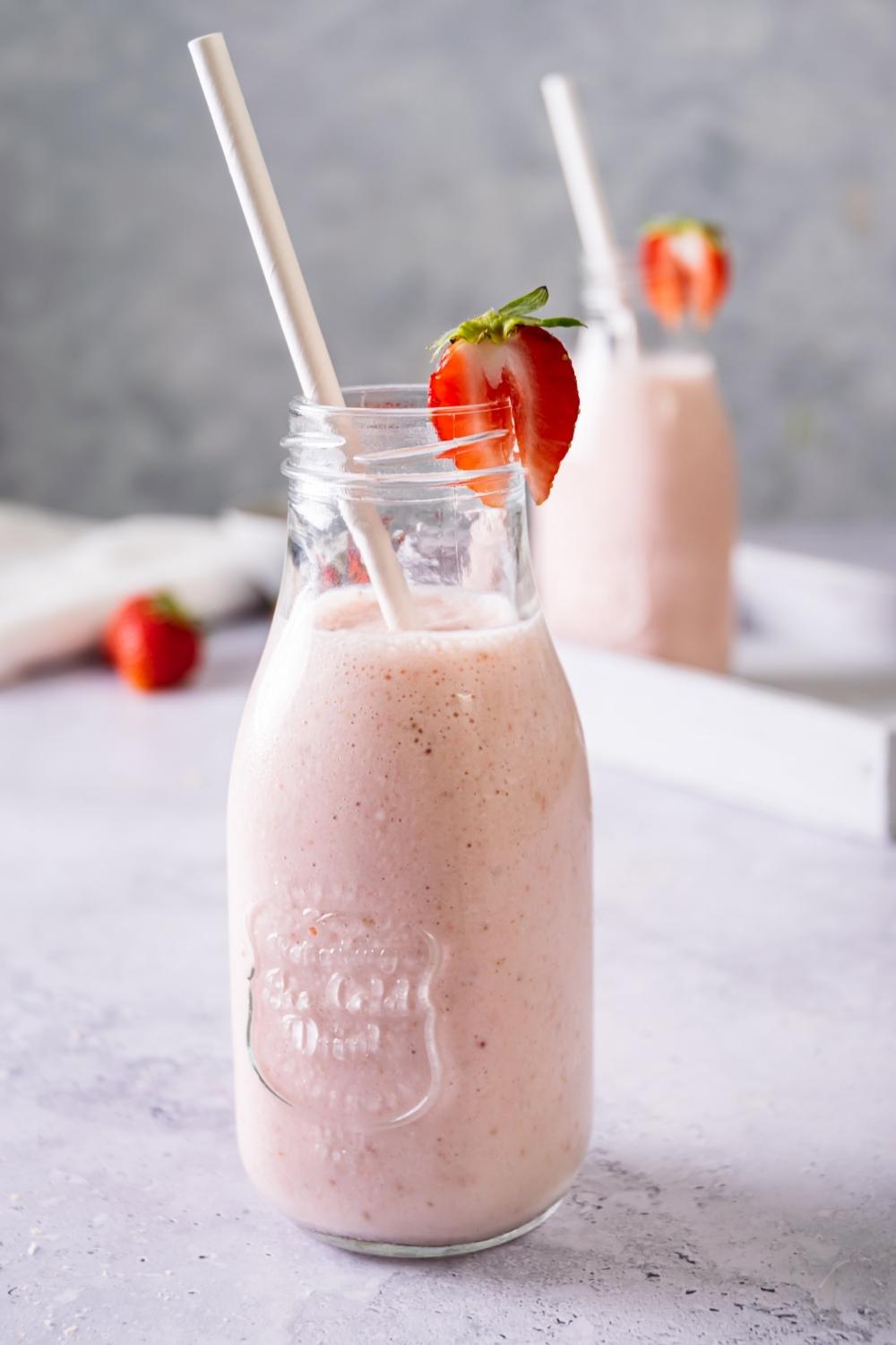 A strawberry banana smoothie in a glass with a straw in it and sliced strawberry on the rim.