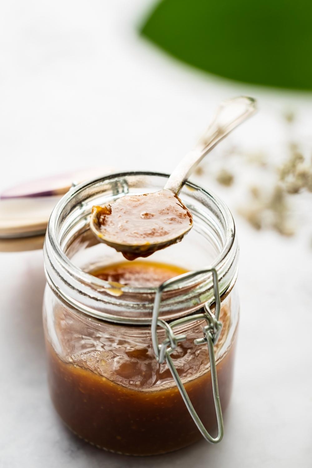A spoon with mcdonalds sweet and sour sauce on it over a glass jar filled with the sauce.