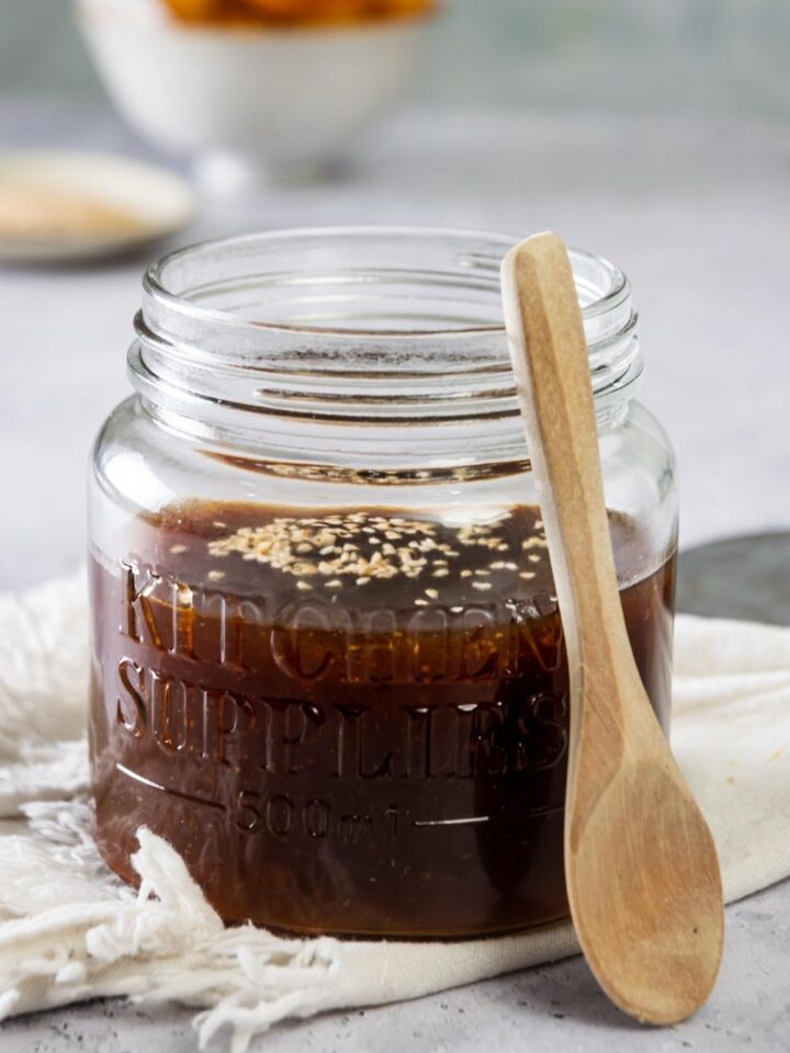 A glass jar filled with szechuan sauce. A wood spoon is leaning against the jar.