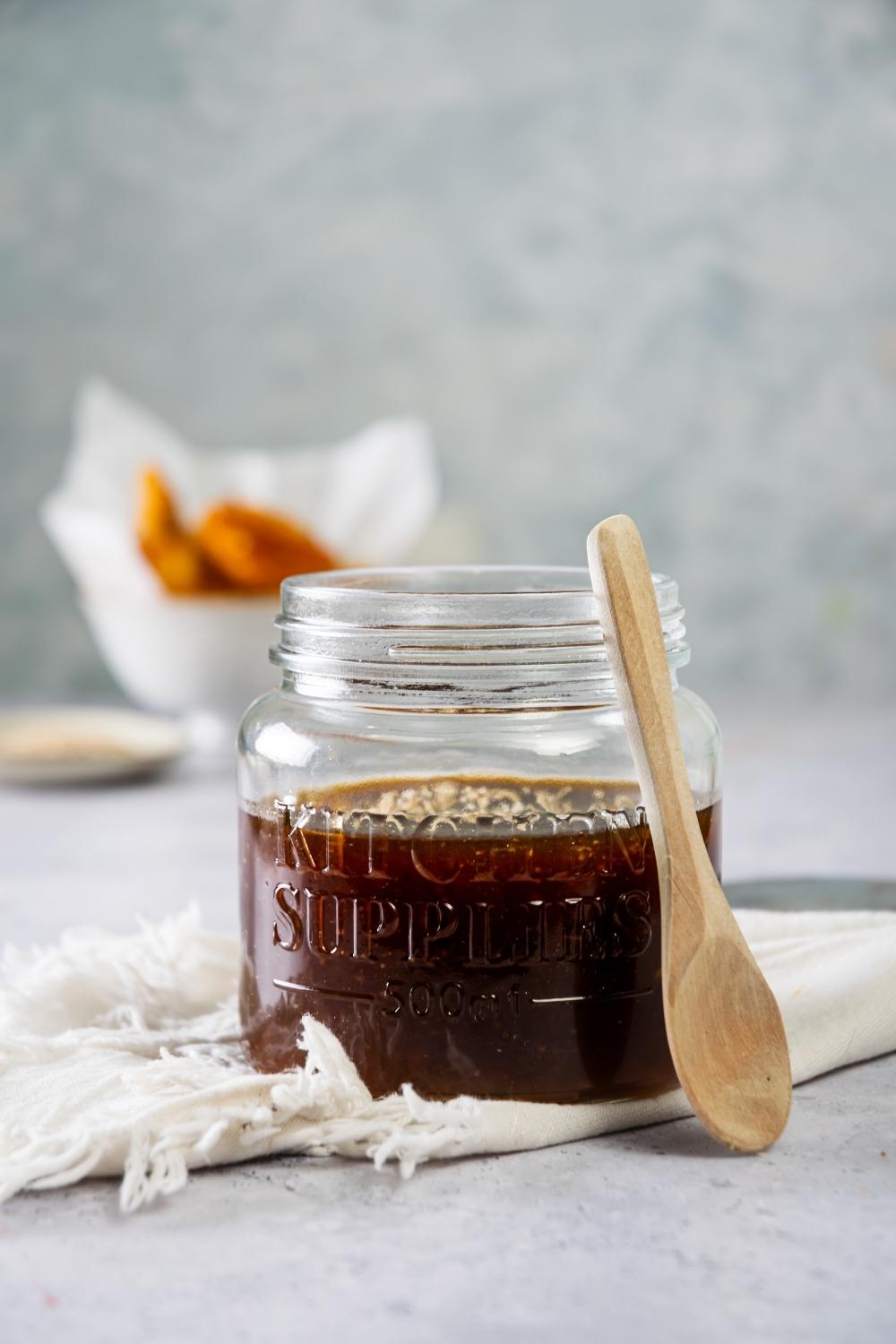 A glass jar that is filled with mcdonalds szechuan sauce with a wooden spoon leaning against it.