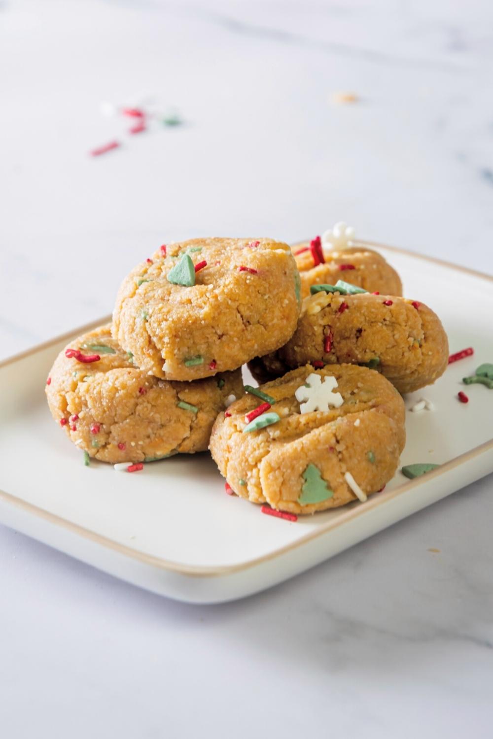 Five no bake peanut butter cookies with red, white, and green sprinkles in them on a white plate.