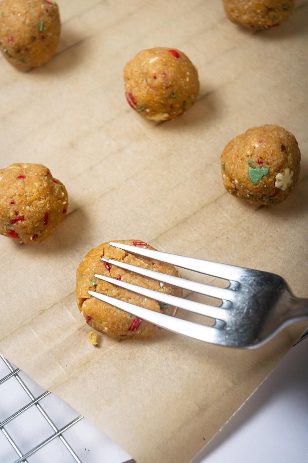 A fork pressing down on a no bake peanut butter ball on a piece of parchment paper. There are three peanut butter balls behind it.
