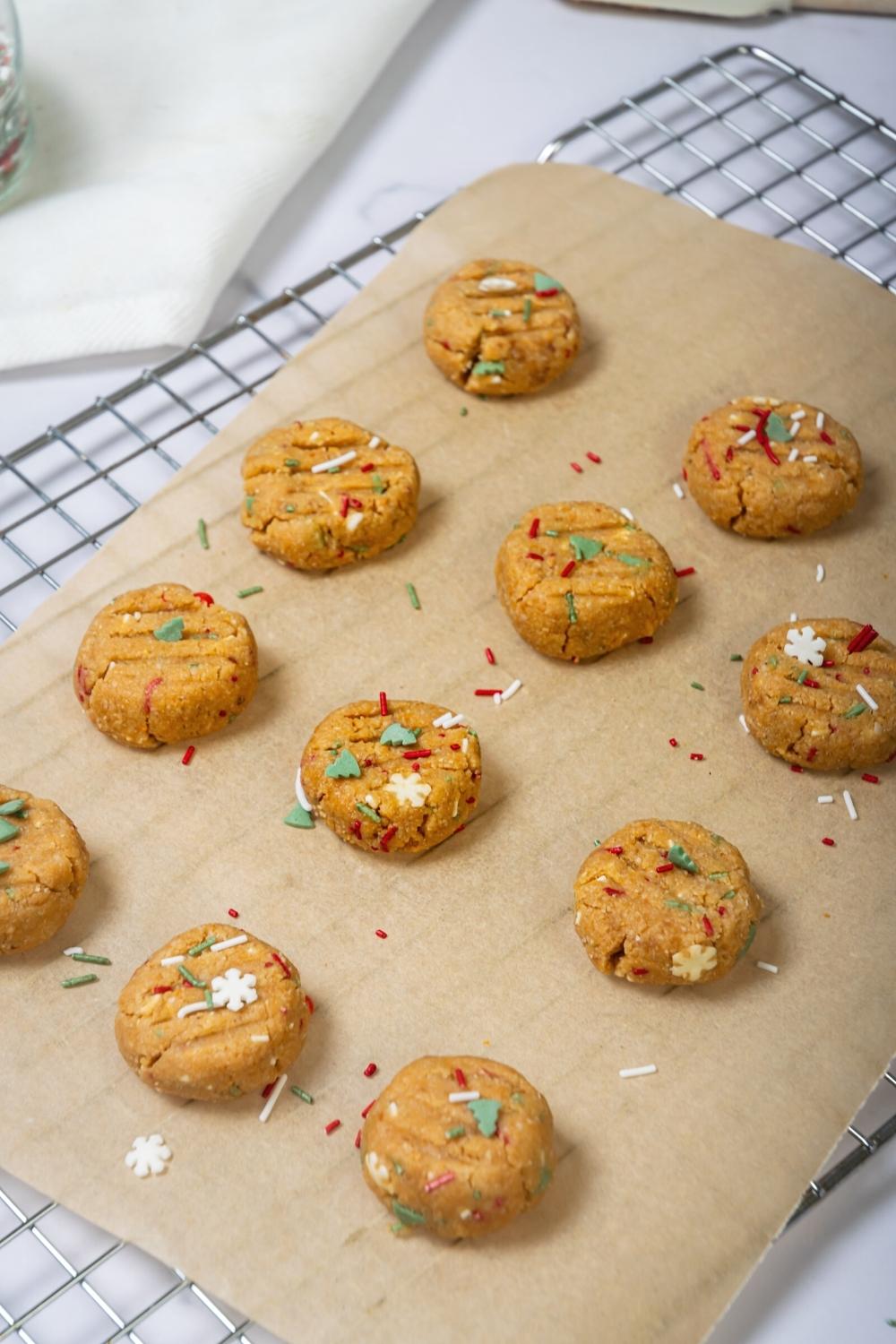 Three rows of four no bake peanut butter cookies with red, white, and green sprinkles on them on a sheet of parchment paper on a wire rack.