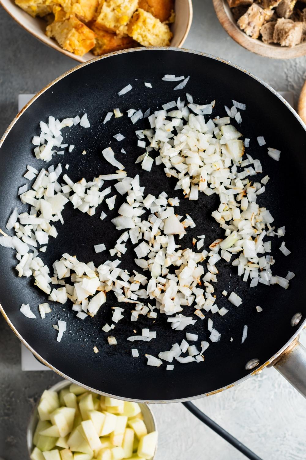An overhead view of diced onions in a frying pan being cooked.