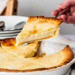 A hand holding a slice of ricotta pie over the whole ricotta pie.