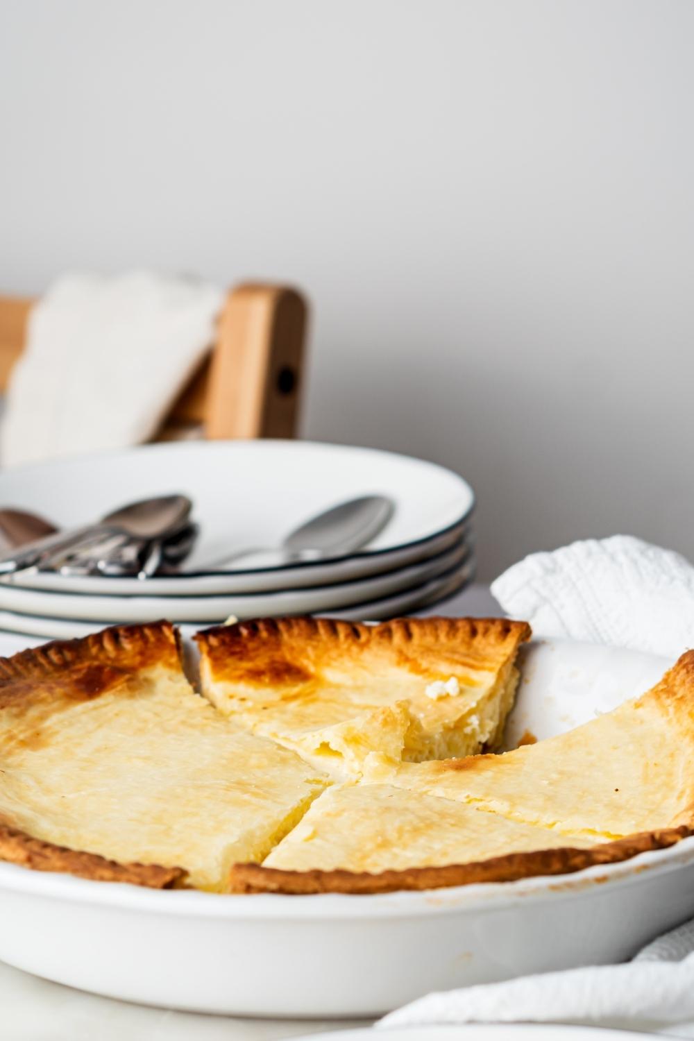 A whole ricotta pie with one piece missing from it in a pie dish.