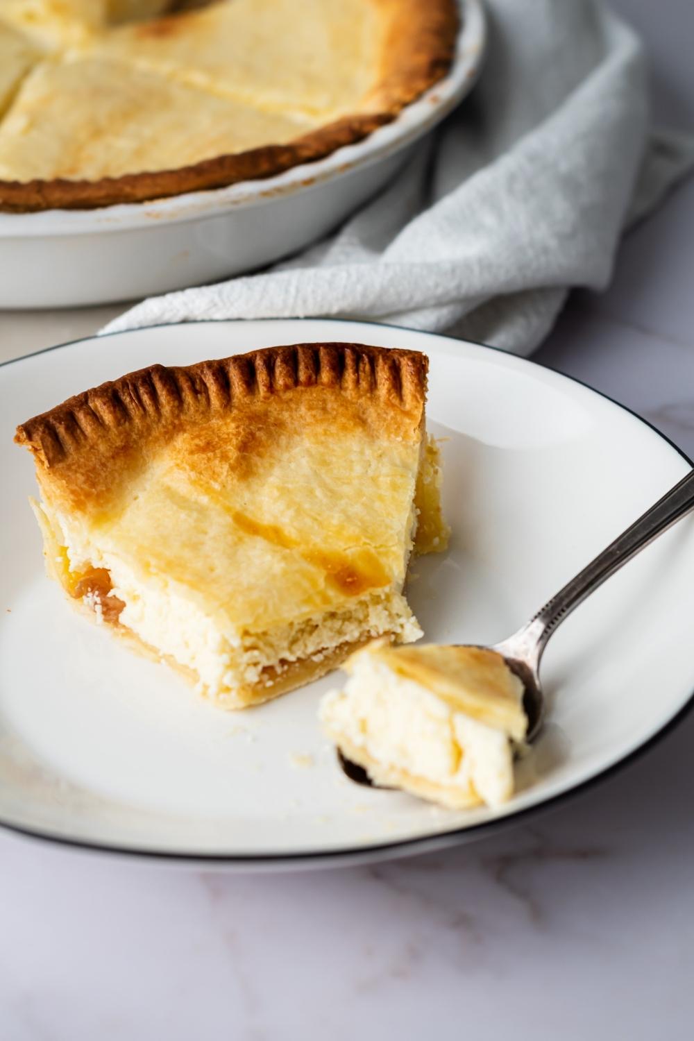 A slice of ricotta pie with a piece out of the front on a white plate. A spoon is on the plate with the piece of the pie on it.
