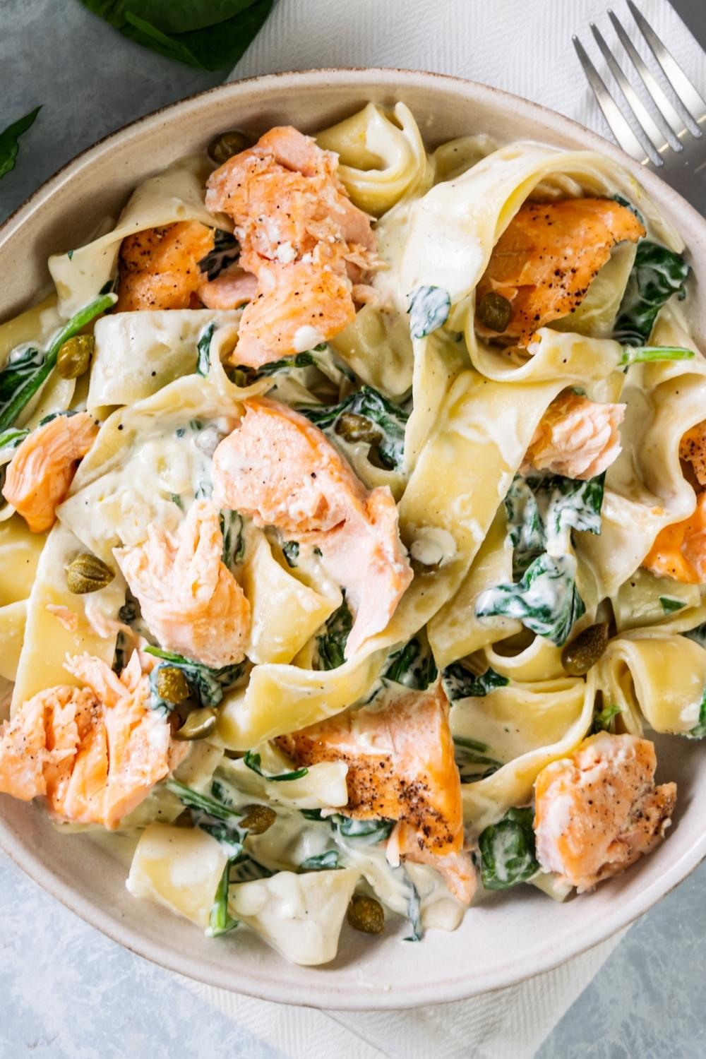 Salmon, spinach, and pasta covered in cream sauce in a white bowl.