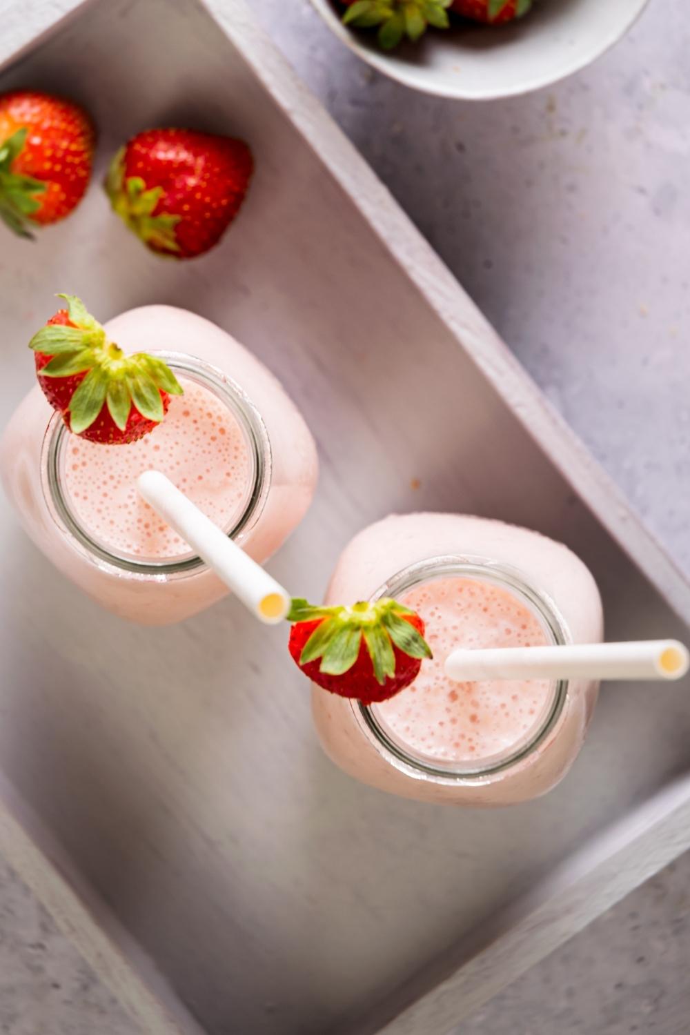 Two glassed with straws in them filled with strawberry banana smoothie.