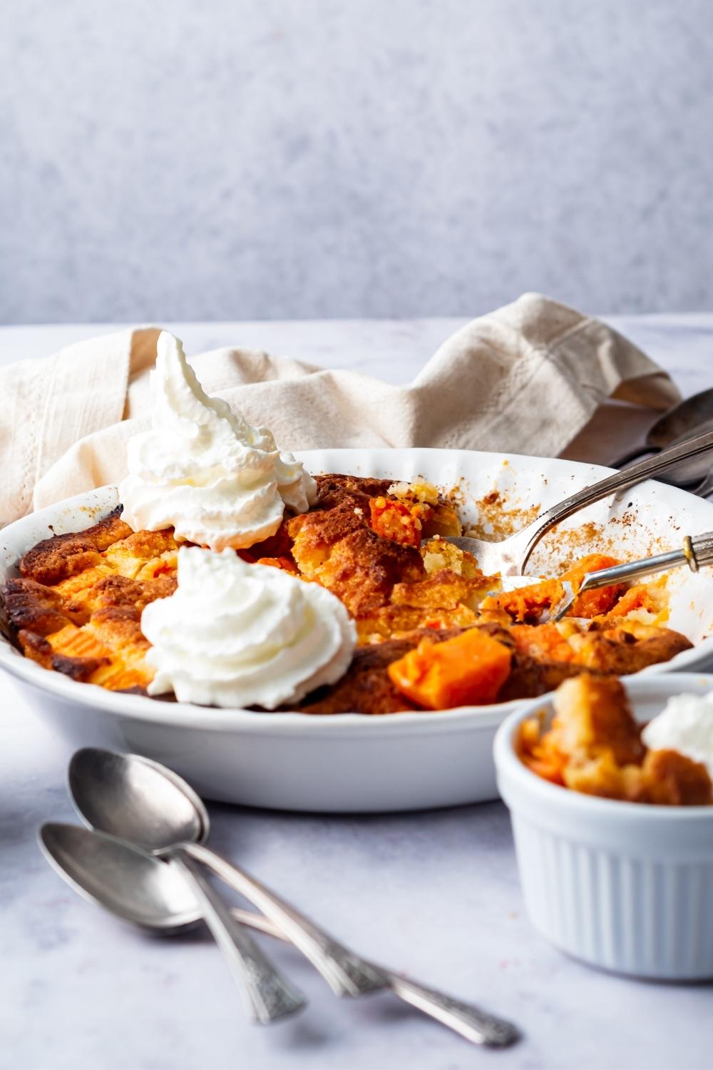 Two dollops of whipped cream on top of sweet potato cobbler in a white pie dish.