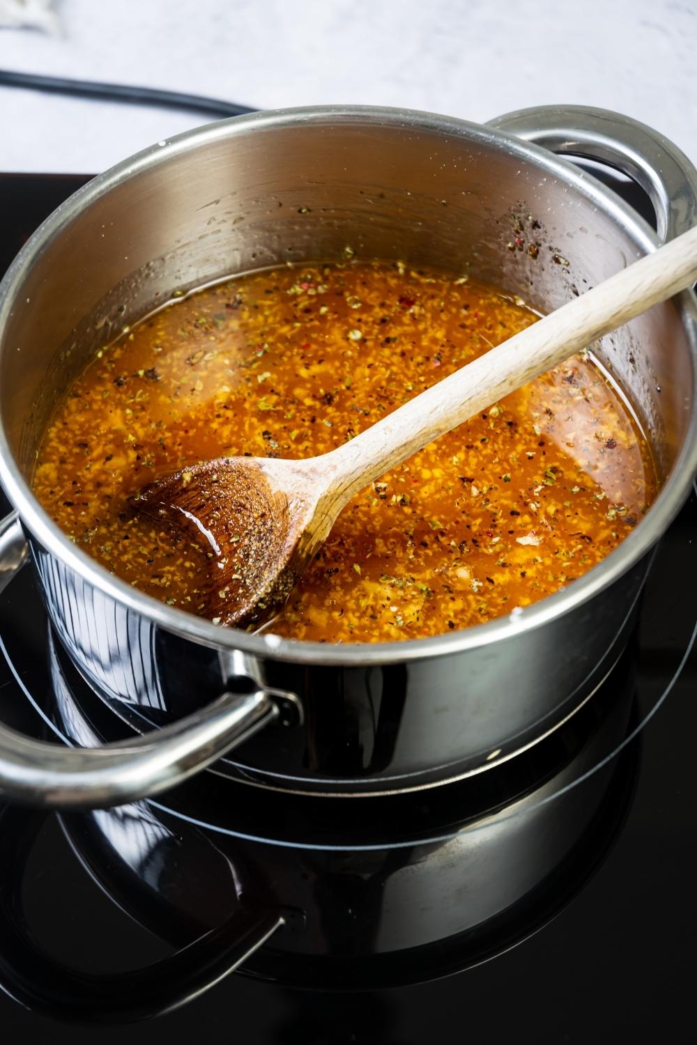 Szechuan sauce ingredients in a pot over a burner with a wooden spoon in it.