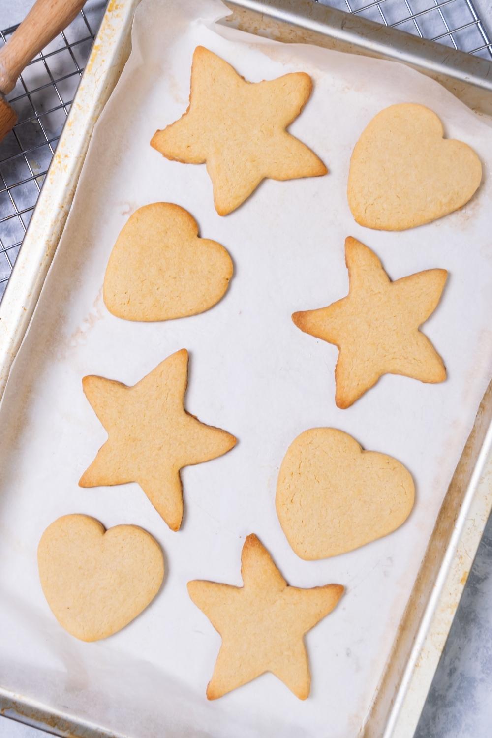 A baking tray lined with parchment paper with baked cut out cookies on it.