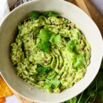 A bowl of homemade chipotle guacamole garnished with parsley served on a wooden cutting board.