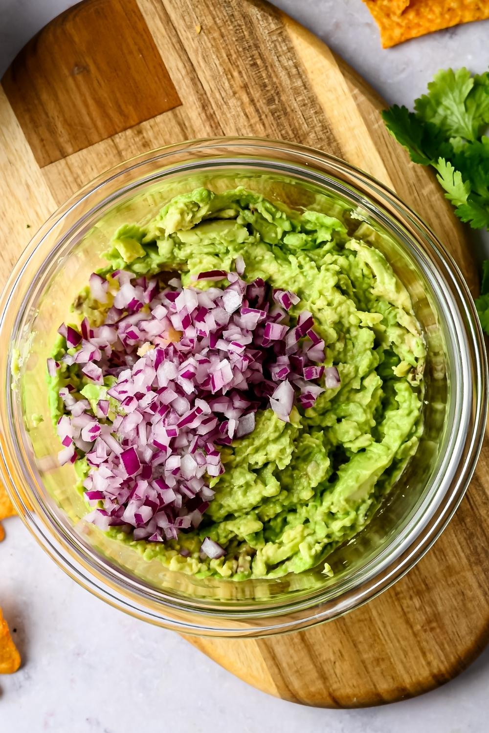 A bowl with smashed avocado, diced onion has just been added to it.