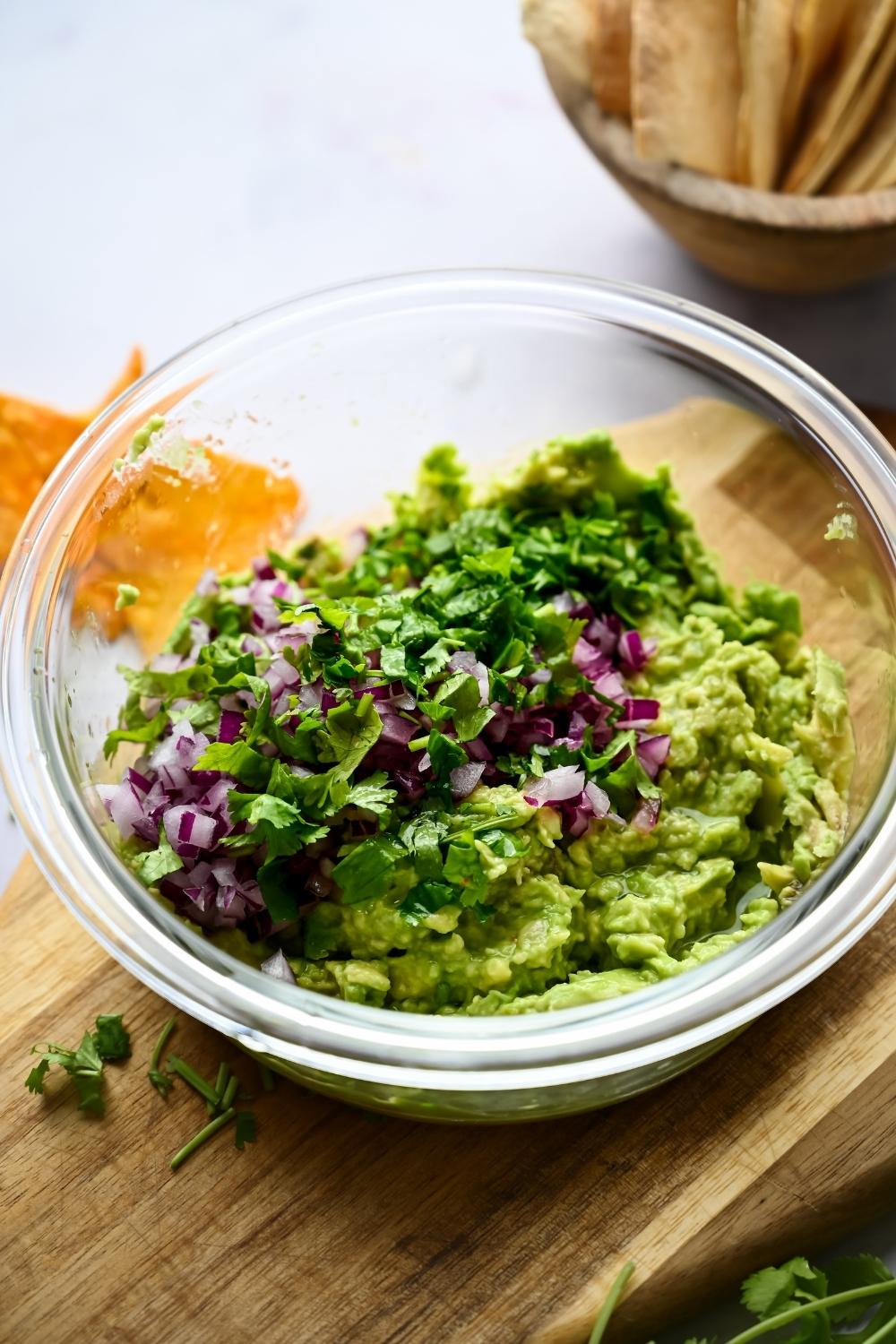 A bowl with smashed avocado, diced onion, salt, and cilantro has just been added to it.