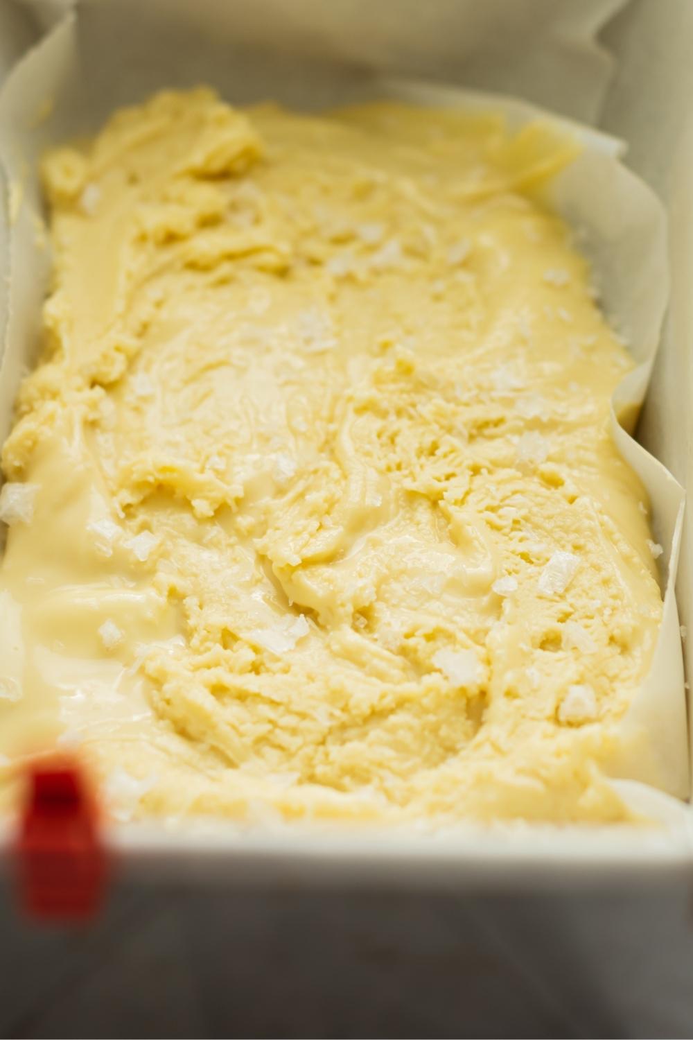 A loaf pan lined with parchment paper with homemade maple fudge in it topped with sea salt.