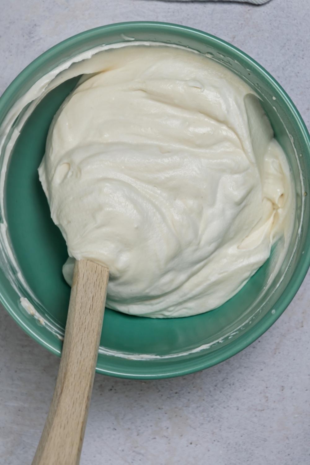 An overhead view of a mixing bowl with a creamy mixture of all the filling ingredients folded by a rubber spatula in the bowl.