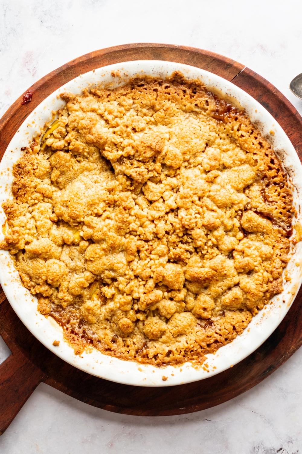 Apple crisp in a baking dish that is on top of a wooden cutting board.