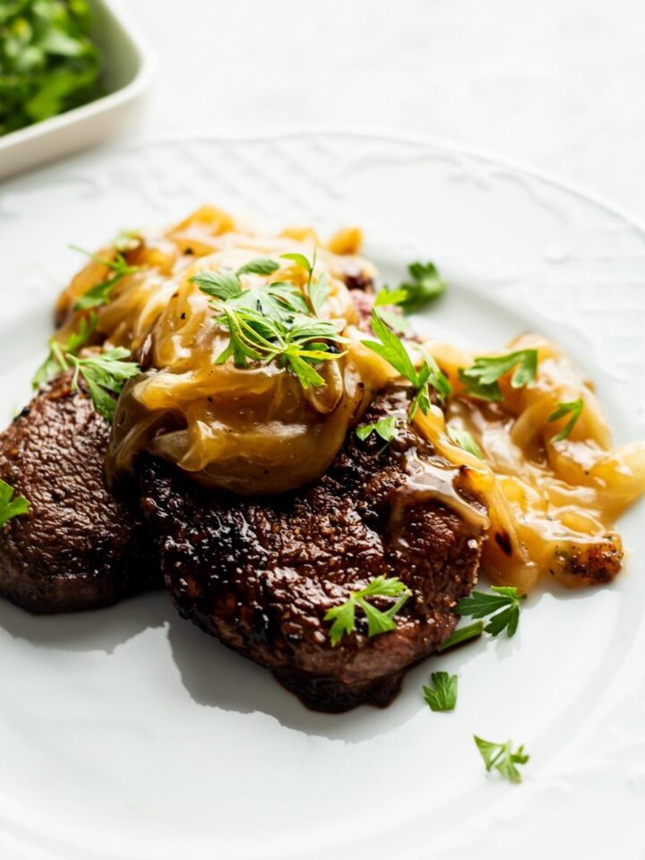 cubed steak with onion gravy and parsley on a white plate