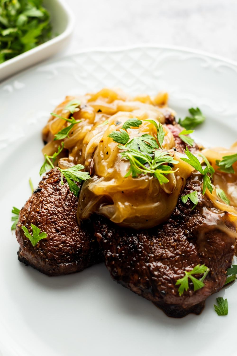 cubed steak topped with onion gravy and parsley on a white plate