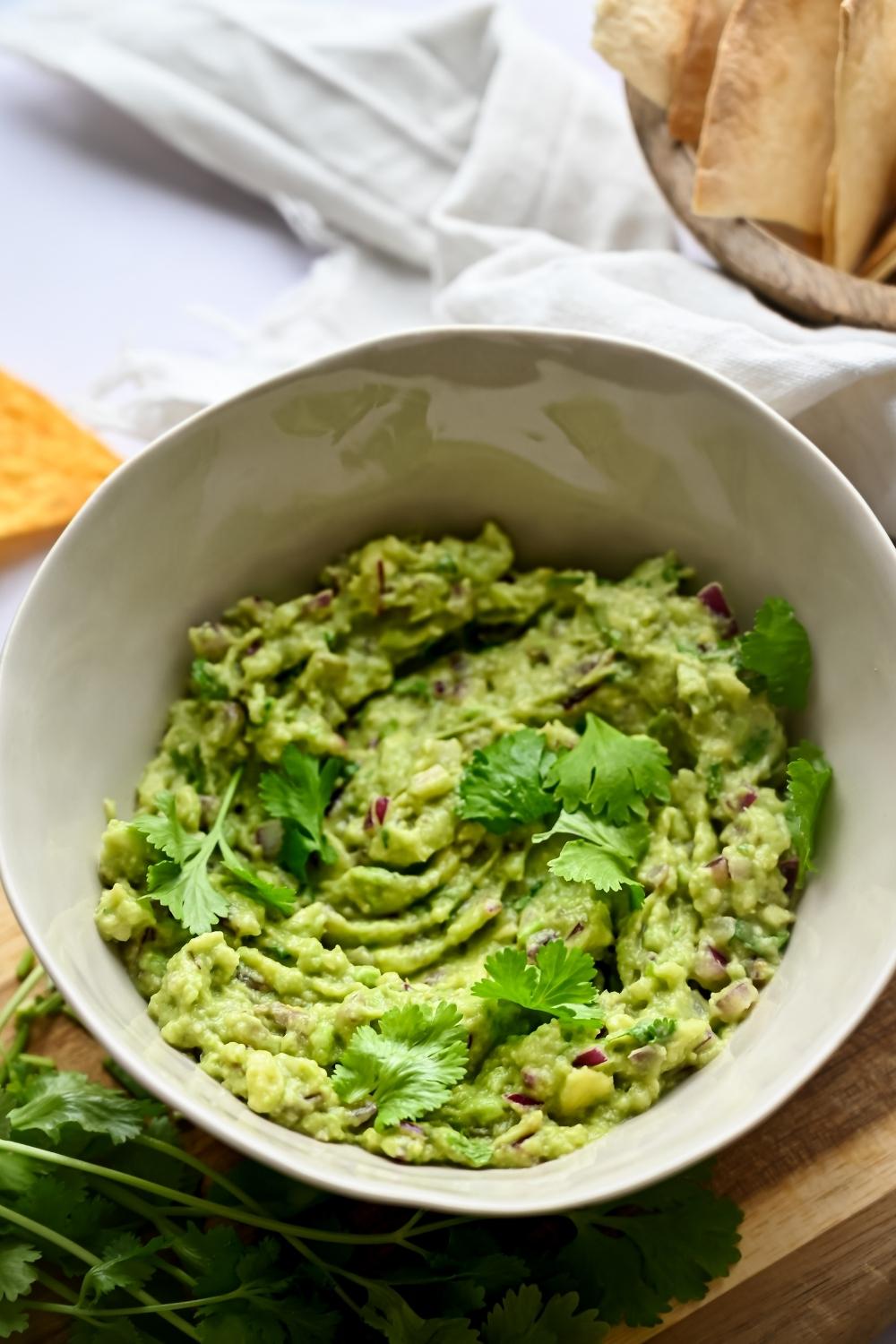 A bowl of homemade chipotle guacamole garnished with parsley served on a wooden cutting board.