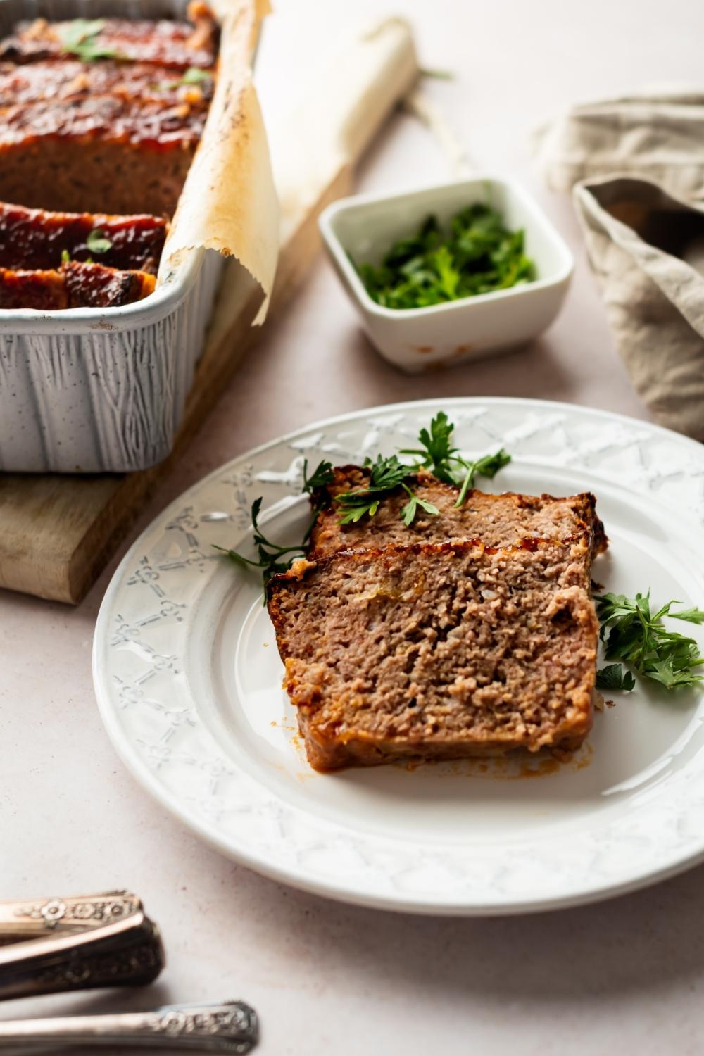 two slices of ham loaf on a plate. the rest of the ham loaf is in the background