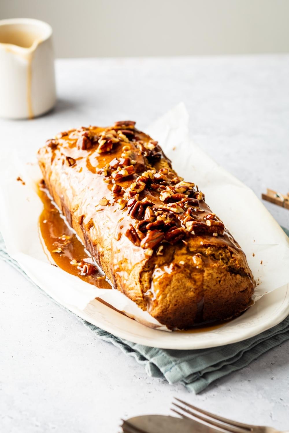 A sweet potato poundcake with pecans and brown sugar glaze on top on a sheet of parchment paper on a white plate.