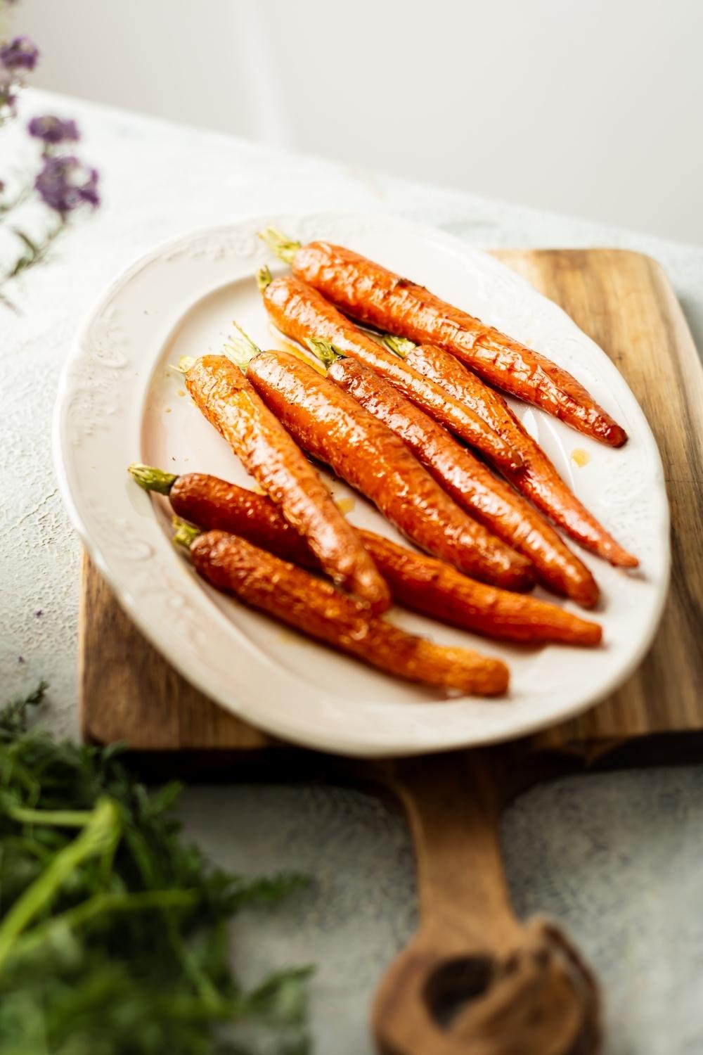 glossy candied carrots on a white plate on top of a wooden board