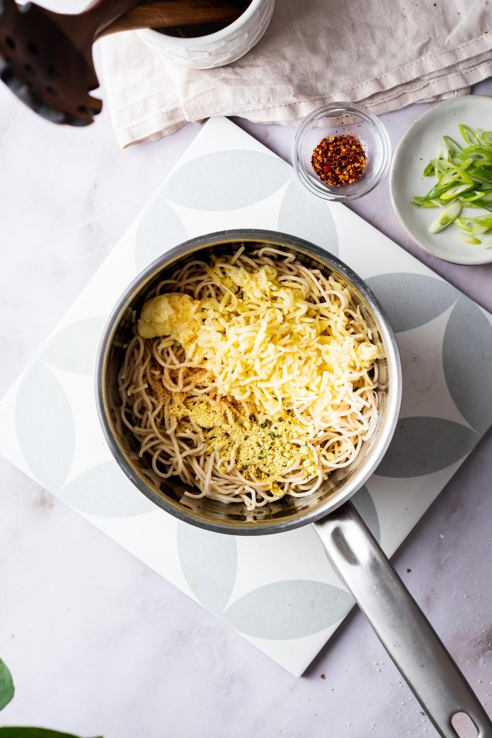 ramen in a pot topped with seasonings and cheese