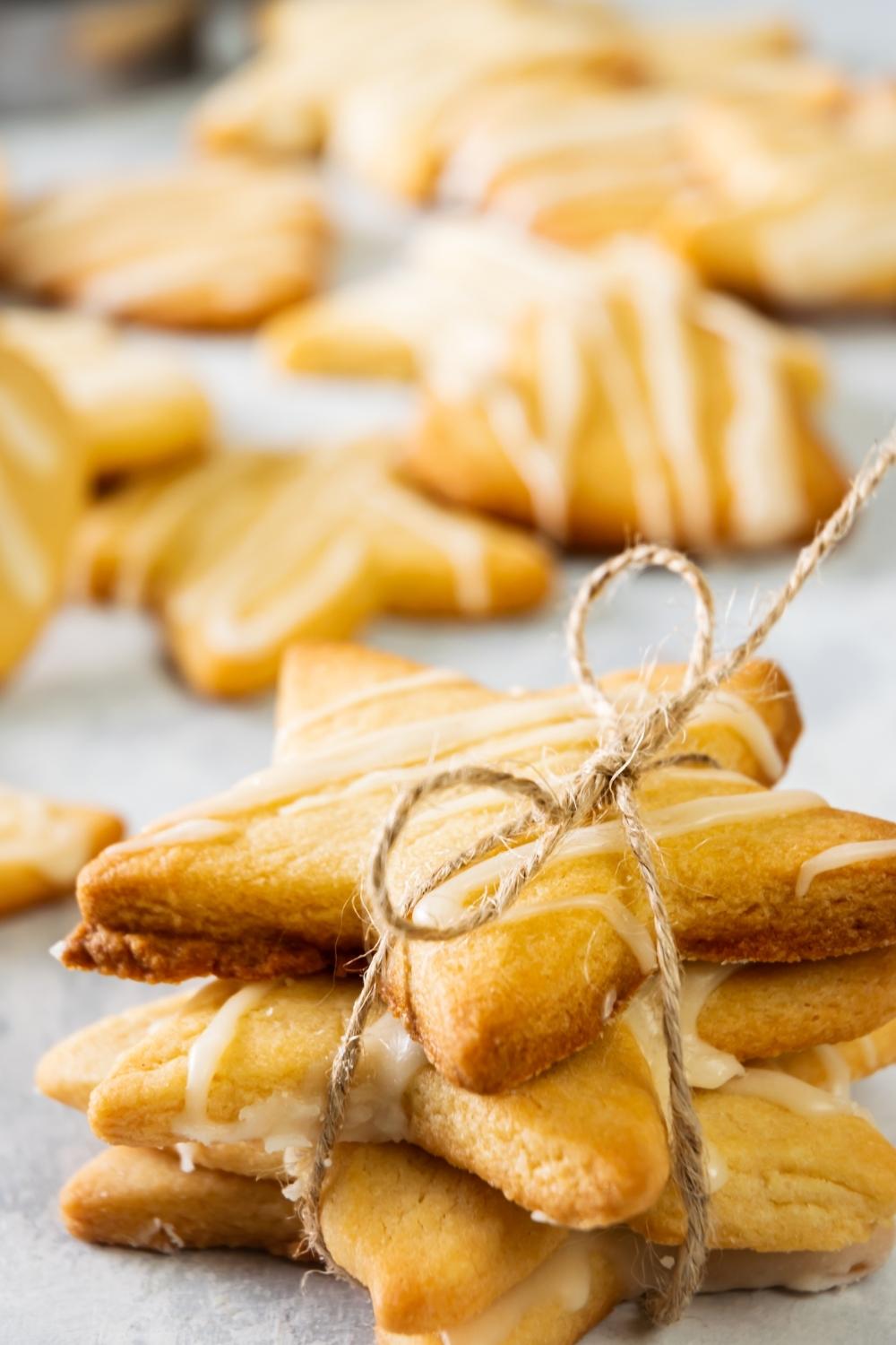 A close-up of a stack of four cut out cookies tied with twine. There are multiple cut out cookies drizzled with royal icing in the background.