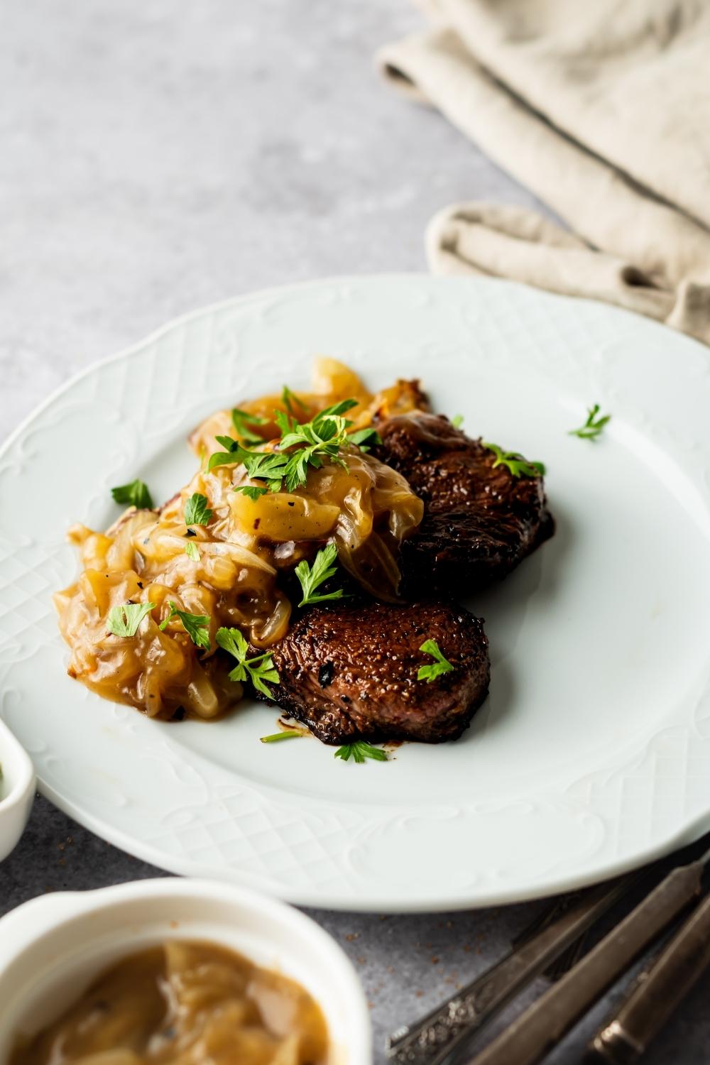 seared cubed steaks topped with onion gravy and parsley on a white plate