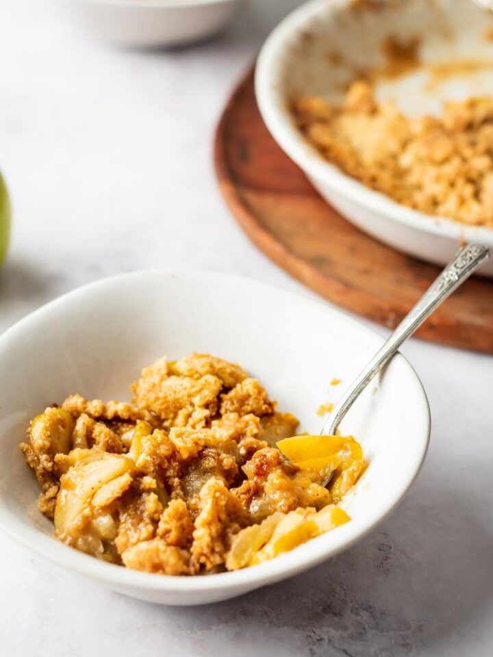 Apple crisp in a white bowl with a fork in it.