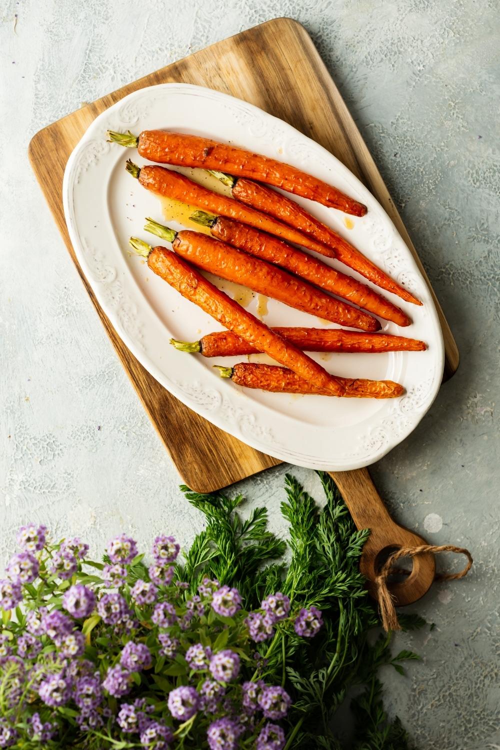 flat lay of candied carrots on a plate with purple flowers on the side