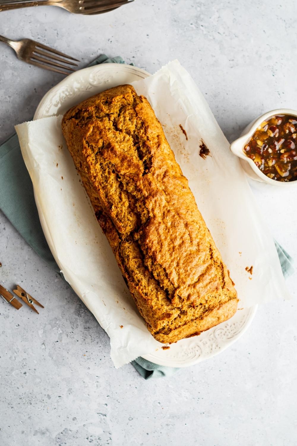 A sweet potato poundcake on top of a piece of parchment paper on a white oval dish.