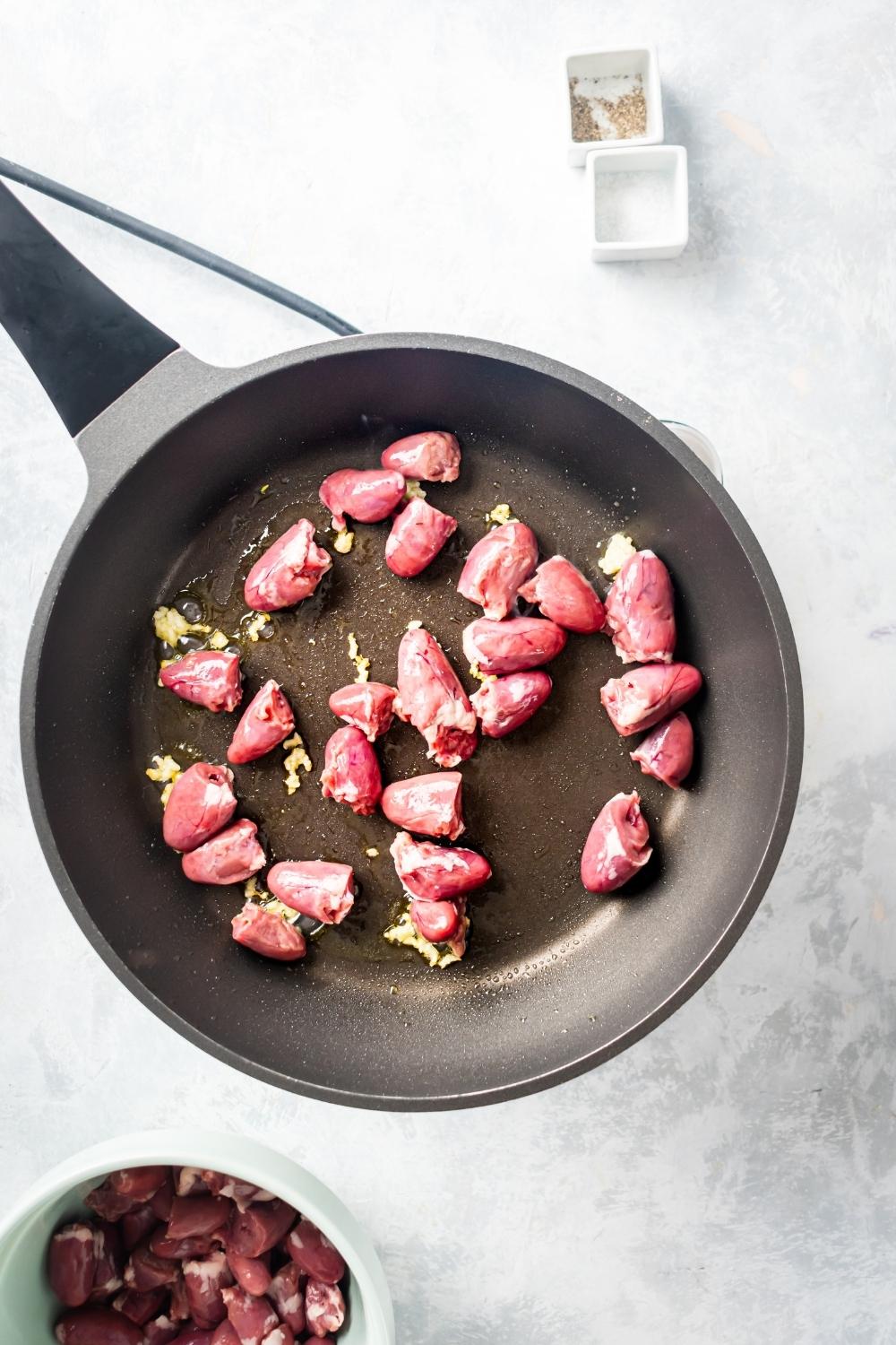 A bunch of chicken hearts in a skillet.