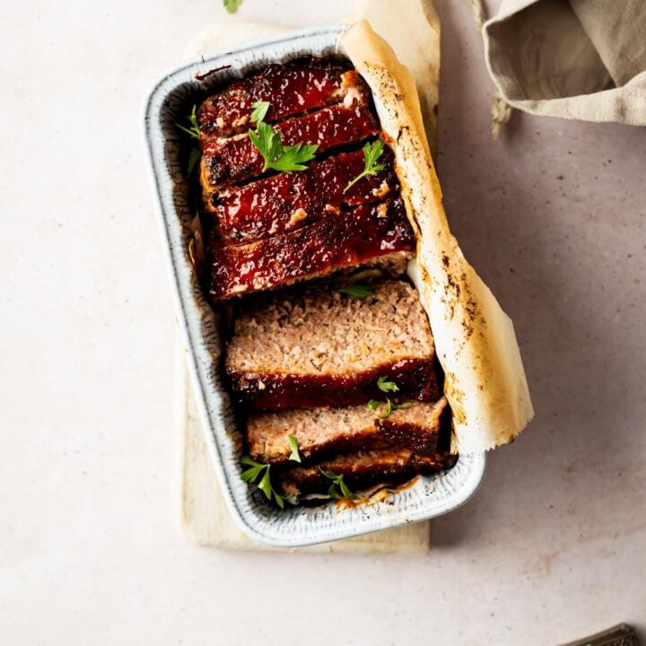 sliced ham loaf in a loaf pan with utensils nearby