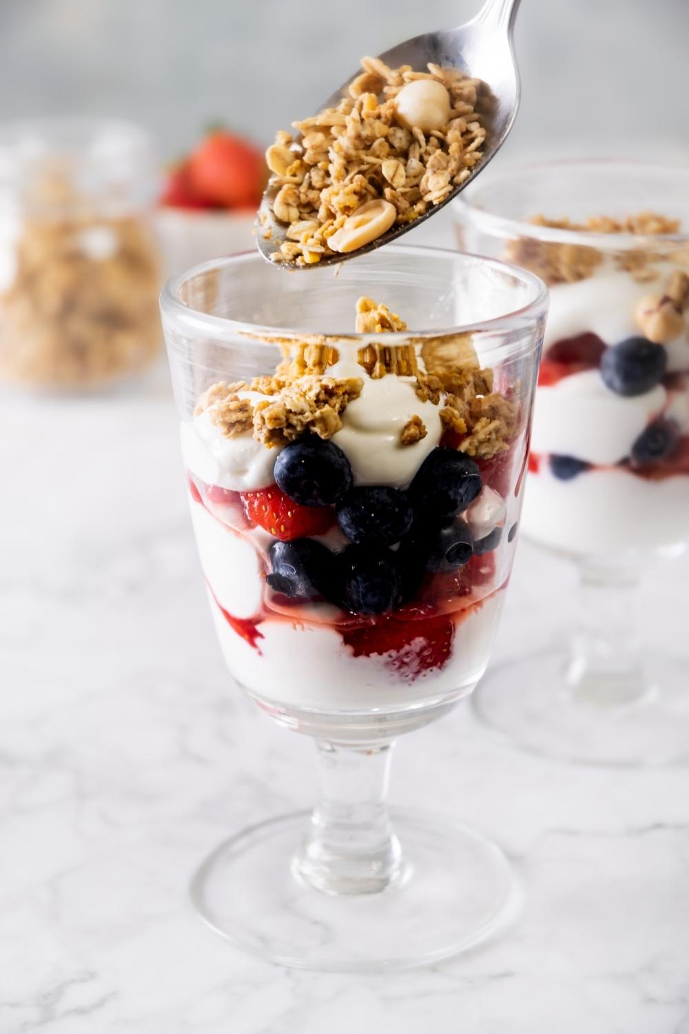 granola being added to a glass of berry yogurt parfait