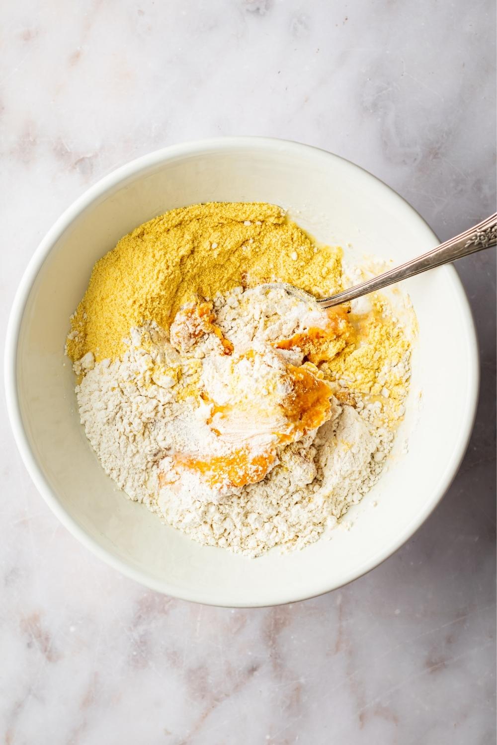 Flour, mashed sweet potato, and cornmeal in a bowl with a spoon in it.