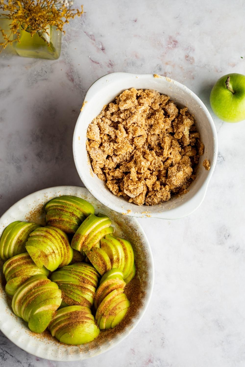 A baking dish filled with sliced apples and a bowl with apple crumble in it.