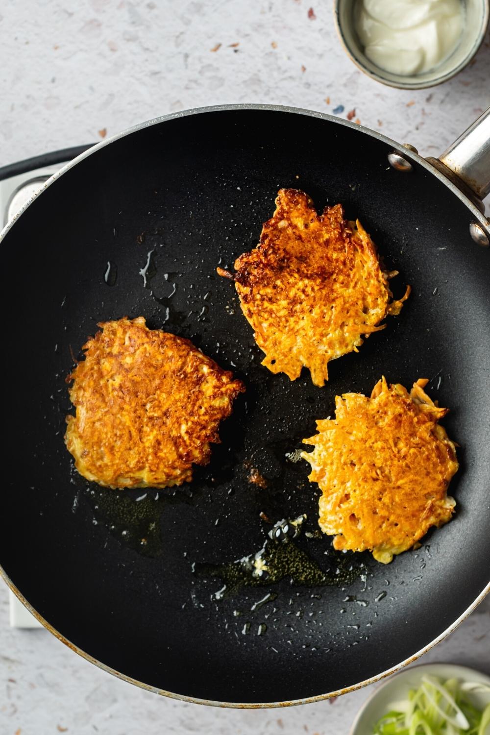 Three sweet potato hash browns on a skillet.