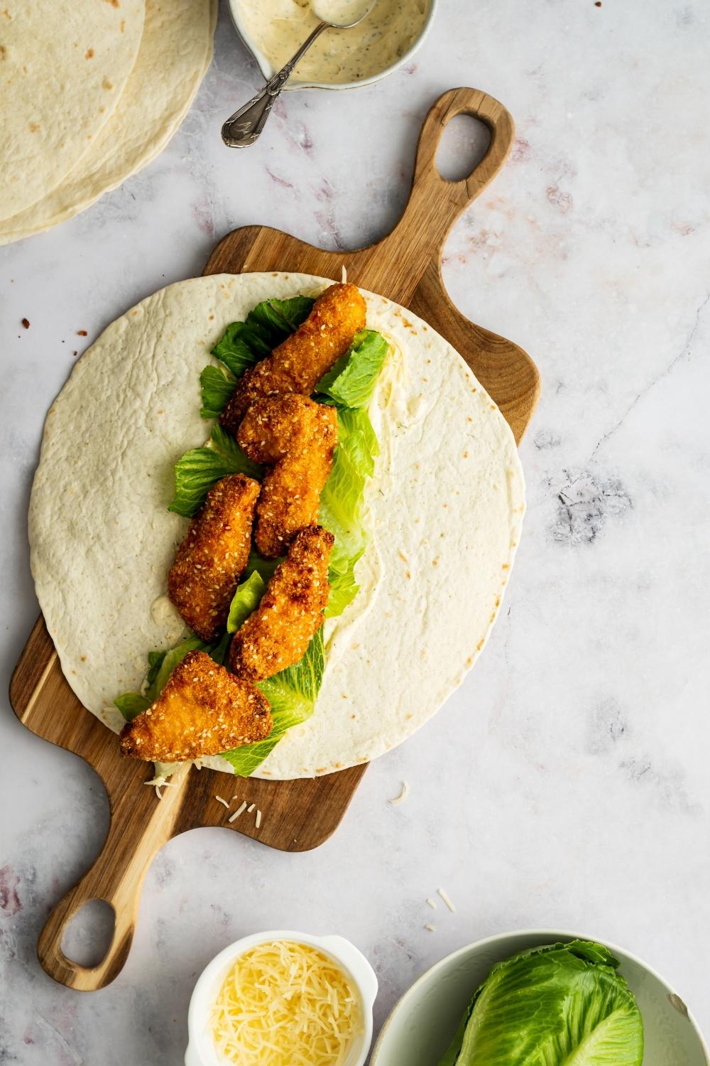 open flour tortilla layered with ranch, lettuce, and chicken tenders